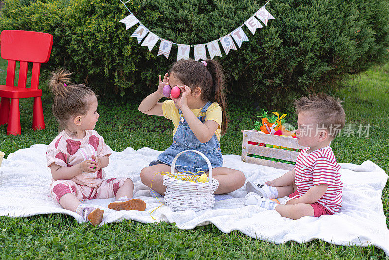 在复活节野餐庆祝活动中，姐姐一边和弟弟妹妹玩，一边用复活节彩蛋做鬼脸
