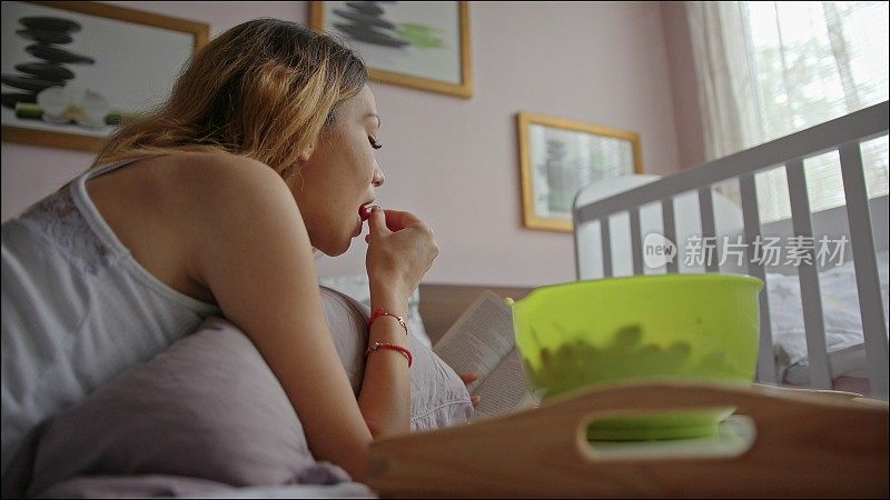 一个女人在卧室的床上一边吃樱桃一边看书。