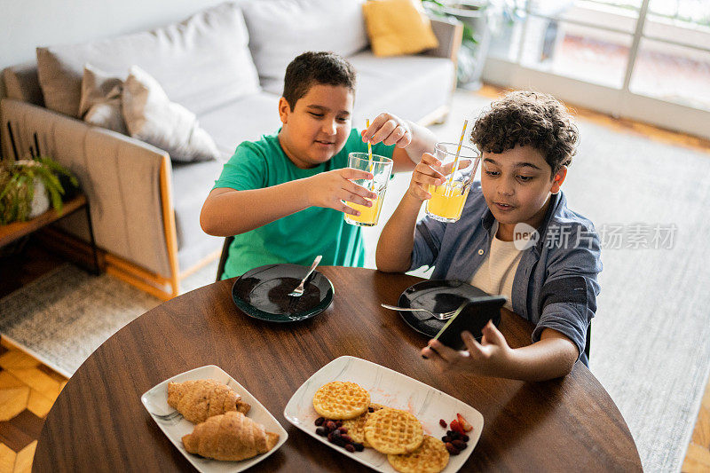 兄弟们在家里的早餐时间用智能手机进行视频通话或拍摄