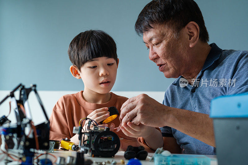 亚洲男孩在家里和爷爷一起制作机器人玩具