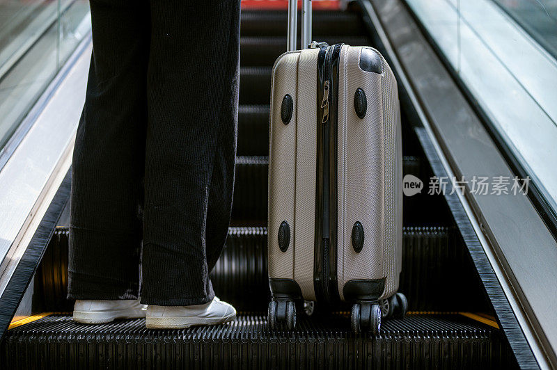 女性在机场乘坐自动扶梯。她拿着行李，准备开始一场新的旅行冒险。