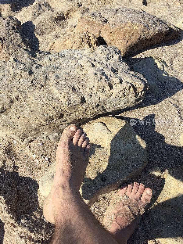 人的脚踩在沙滩上的沙子和石头上