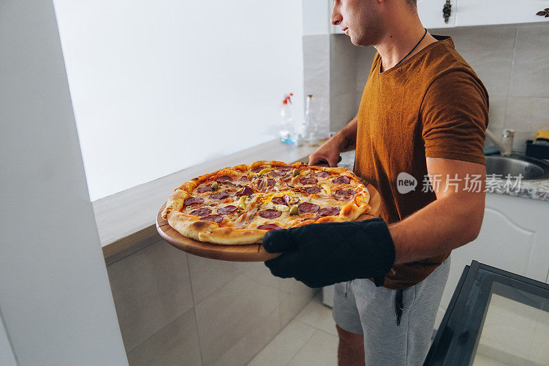 男子在厨房准备披萨，从烤箱取出披萨和服务