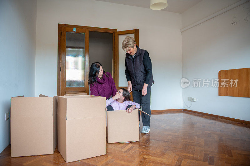 搬到一个新的家庭概念。小女孩在纸板箱里开心地笑着，和她的妈妈和奶奶一起玩。