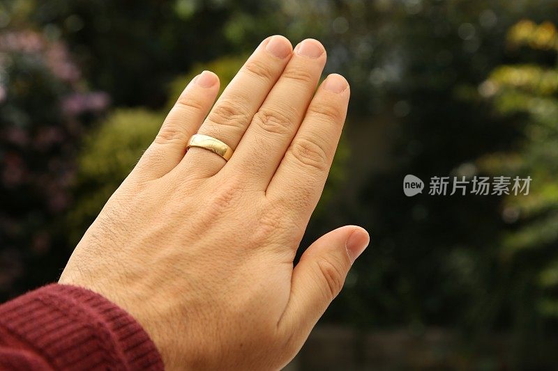 一个人戴着金婚戒指的手特写，自然背景模糊