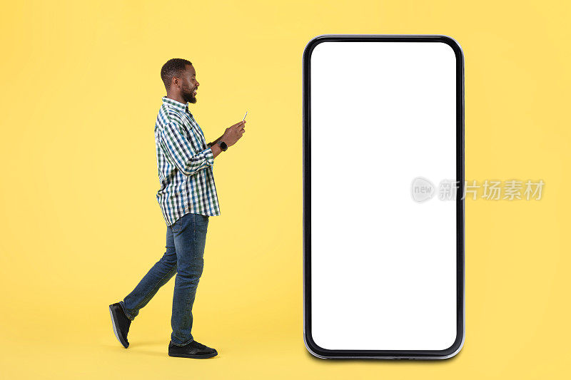 使用智能手机的黑人男子走在巨大的手机旁，黄色背景
