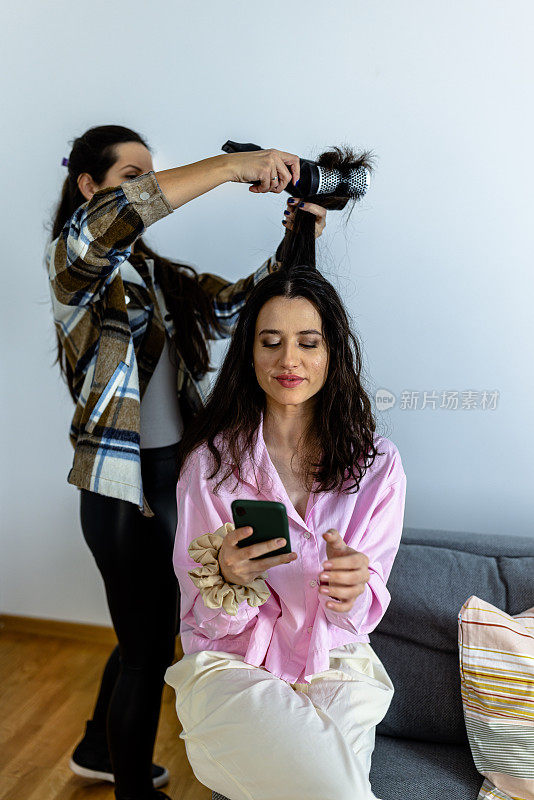 一名女发型师正在一名女子家中使用吹风机。