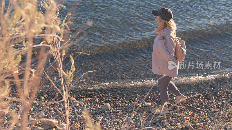 一个成熟的女人背着双肩包走在湖边