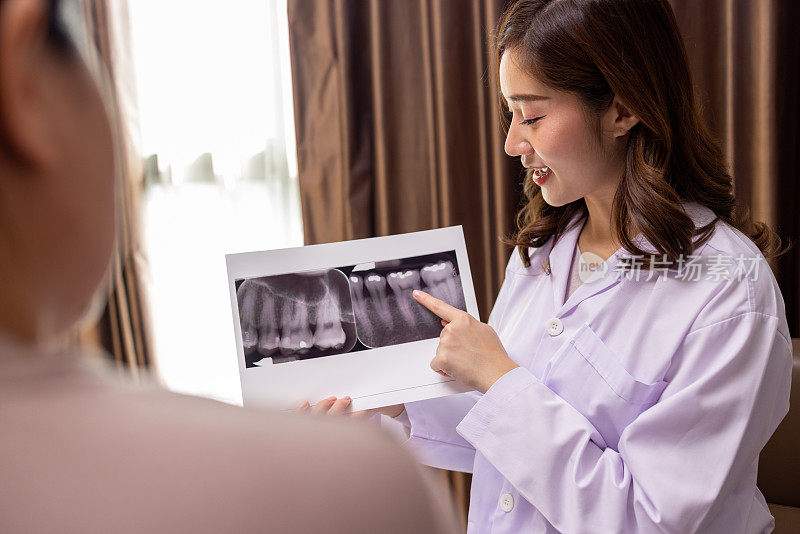 一名亚洲女牙医在接待处与一名拿着牙齿x光照片的病人交谈