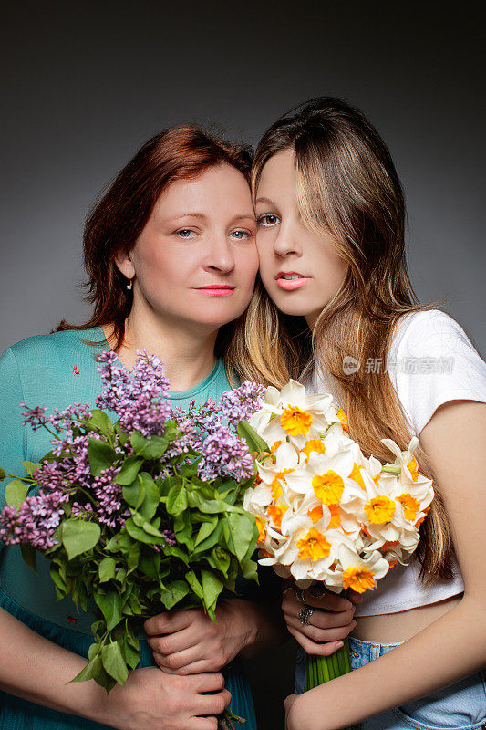 中年妇女站在她十几岁的女儿旁边，两人都拿着花束