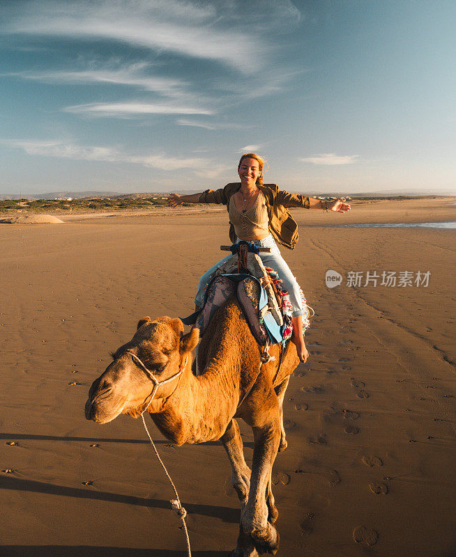 兴高采烈的女人骑着骆驼，兴奋地张开双臂