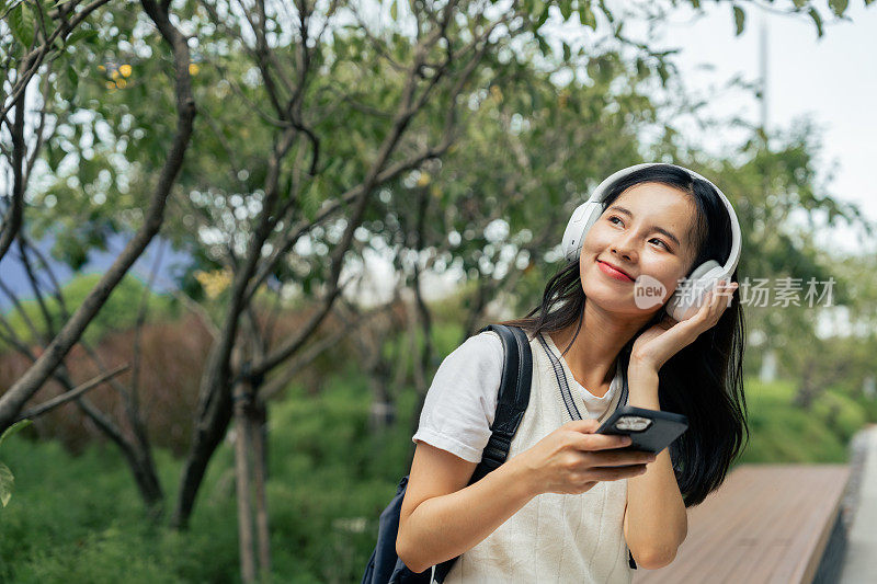 微笑的女人用智能手机和耳机拥抱大自然的旋律