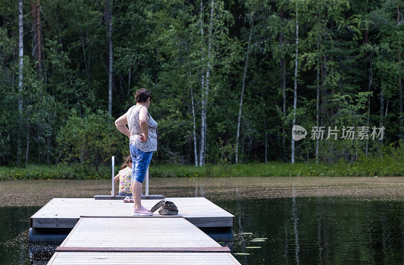 一个77岁的老妇人和一个8岁的白人女孩在森林湖的木码头上。奶奶和孙女在度假。