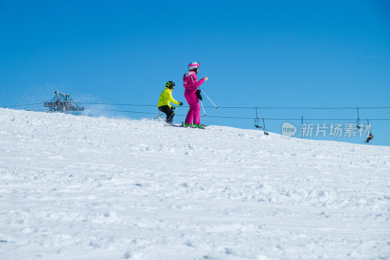 在晴朗的天空下，在白雪覆盖的斜坡上慢慢滑雪下山