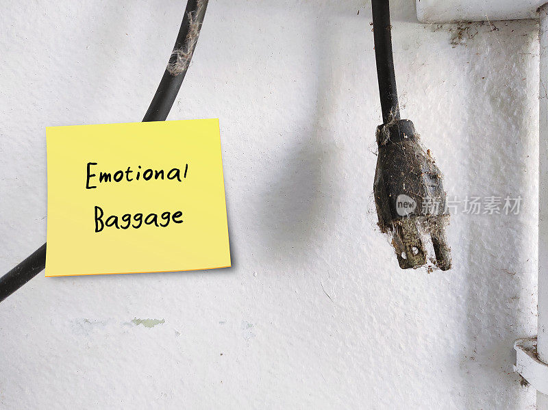 旧的脏电源插头挂在白色的墙上，贴着写有“情感包袱”的便签——背负着过去所有的失望、错误和创伤的概念，背负着过去经历中消极的、未经处理的情绪