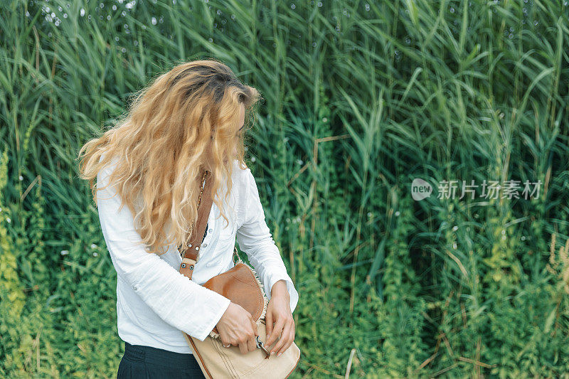 一个卷发的女人在美丽的田野里打开她的包