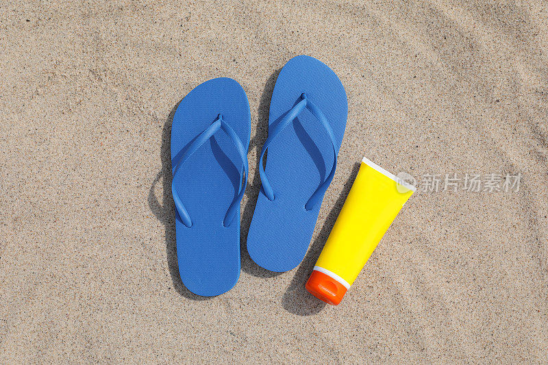 蓝色人字拖和防晒霜放在沙滩上，平躺着