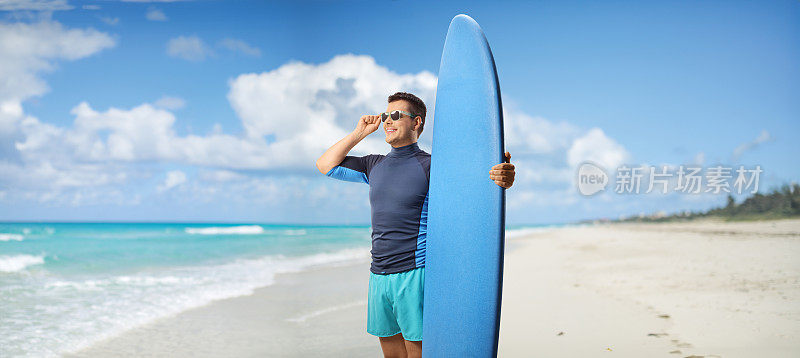 一个带着太阳镜和冲浪板的人站在古巴的海滩上