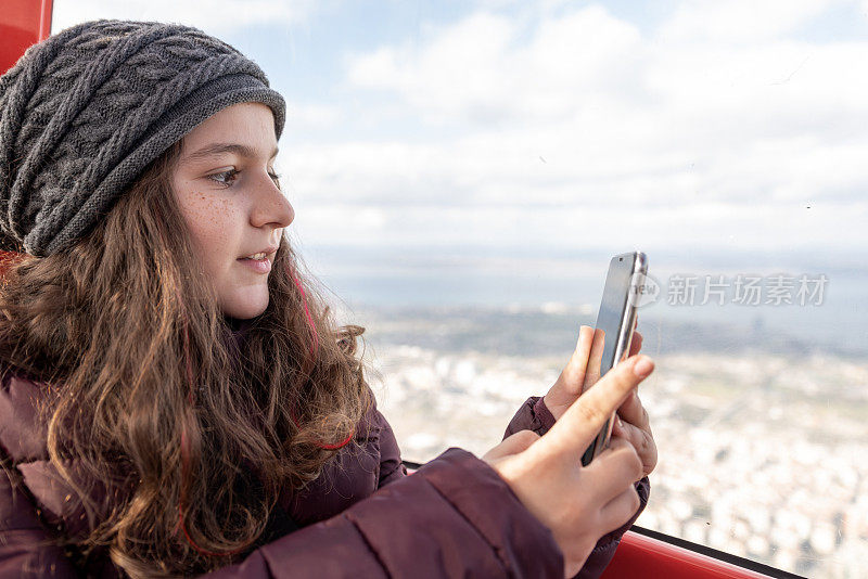 可爱美丽的小女孩，戴着一顶羊毛帽子，在高处的窗户前看着外面