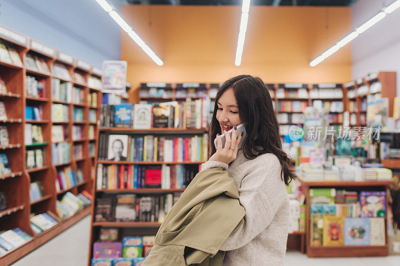 严肃的青少年Z世代韩国女学生拿着手机，在大学图书馆使用智能手机上的app，浏览、聊天、上网咨询，心情愉快、开心、微笑。系列的一部分