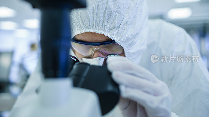 一个科学家穿着防护服在实验室用显微镜和个人电脑做研究的特写镜头。现代制造半导体和制药项目。