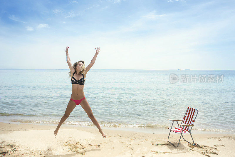 快乐的女人穿着比基尼泳装在海滩上跳