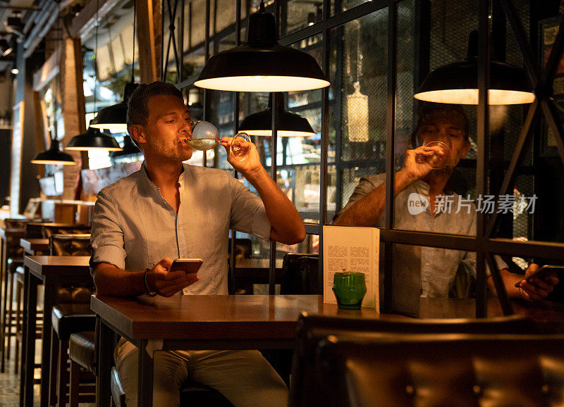 一个男人在餐厅喝酒，用手机