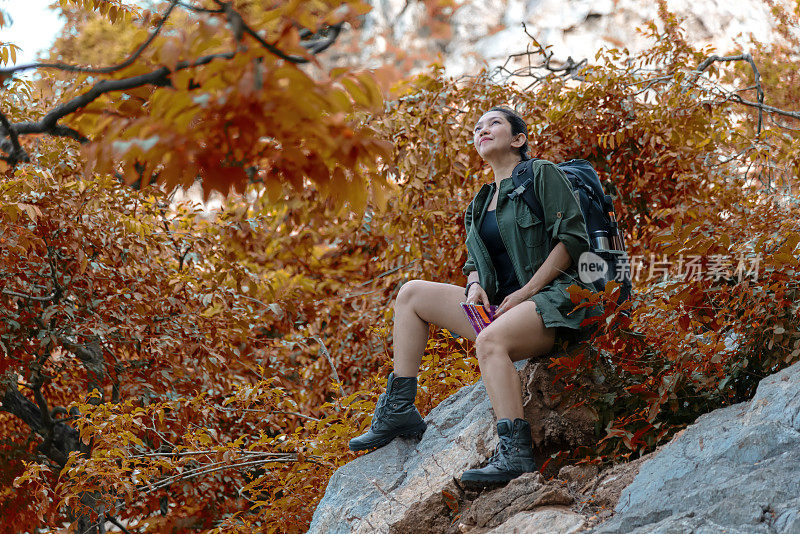 徒步女感觉胜利坐在放松的河边在秋天的森林和露营在假日。旅行的概念。