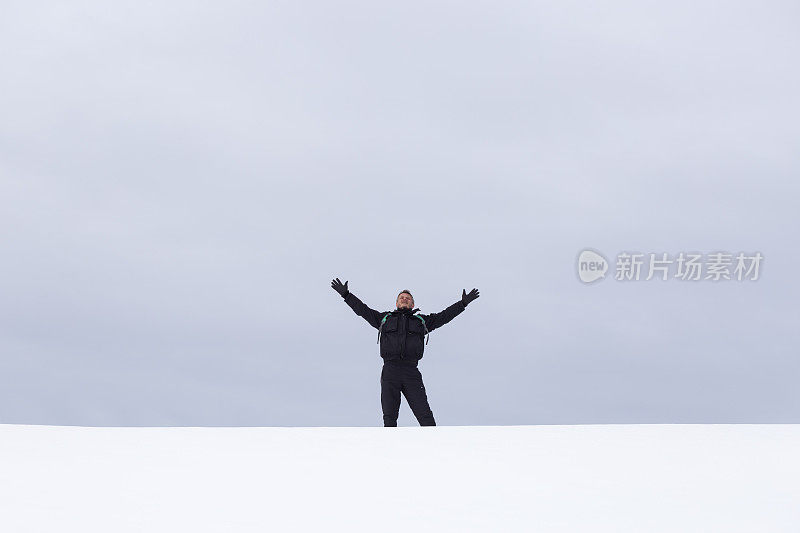 成年男子徒步旅行者张开双臂，望着白雪覆盖的空旷田野