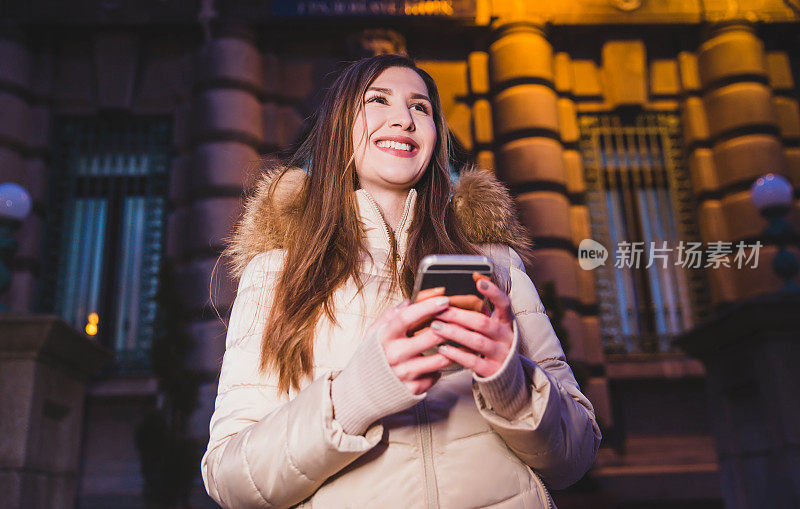 一个女人拿着智能手机站在房前