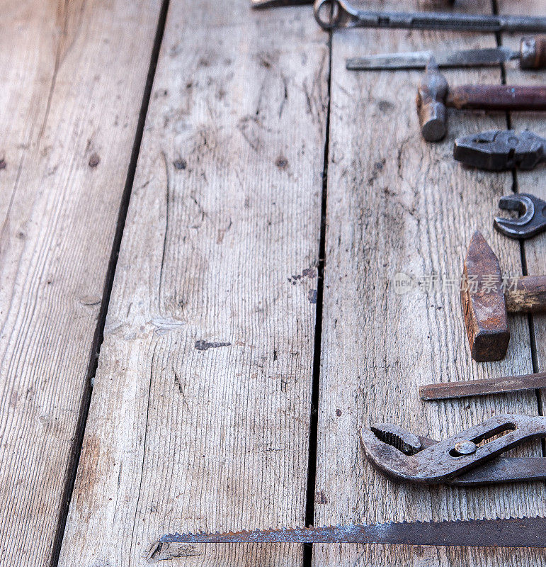 旧的生锈的工具放在一张黑色的木桌上。锤子、凿子、钢锯、金属扳手。本空间