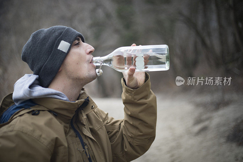 年轻的成年男子在大自然中徒步旅行时喝水