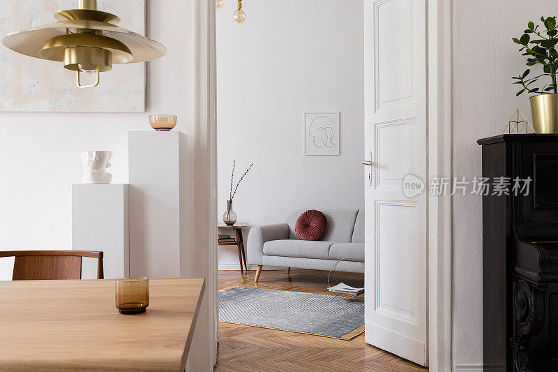现代scandi室内客厅设计的木桌，椅子，沙发和白色支架与时尚的配件。墙上的抽象画。优雅的家居装饰。模拟海报框架。