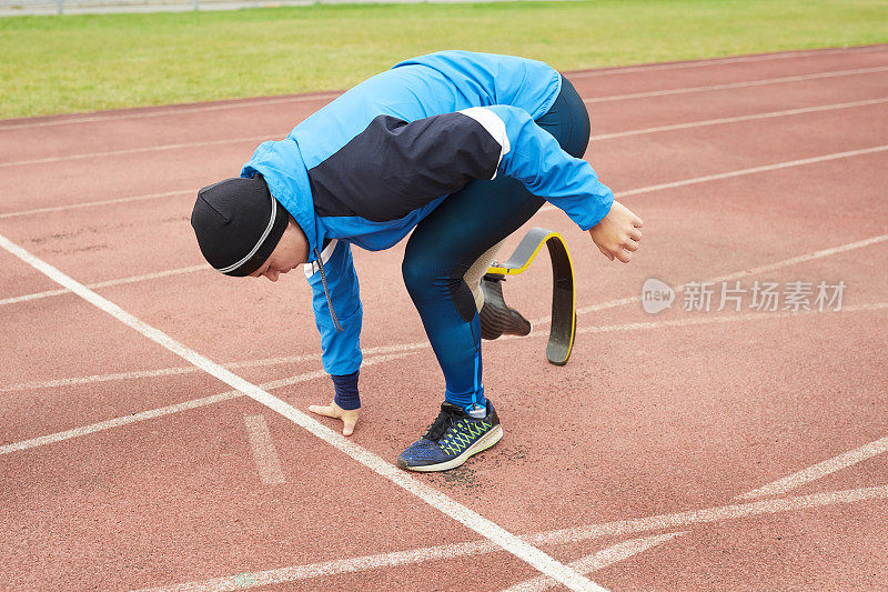 年轻男子运动员用假腿站在起跑位置，倚靠在地上准备跑步