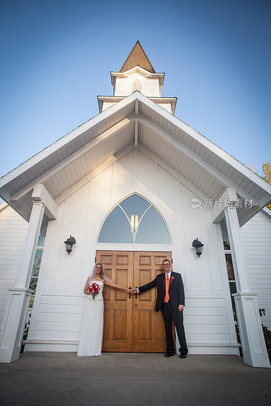 新婚夫妇牵着白色传统教堂木门