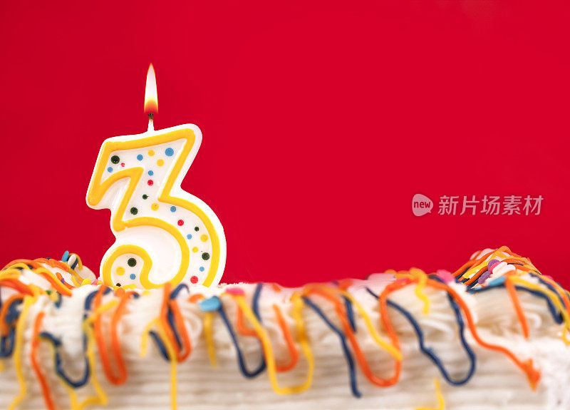 用燃烧的3号蜡烛装饰生日蛋糕。红色的背景。