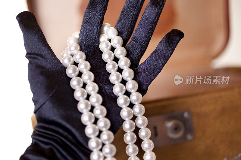 珍珠项链，女士的黑手套，背景是旧行李箱