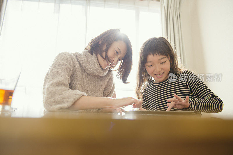 母亲和女儿在家里玩电子平板电脑