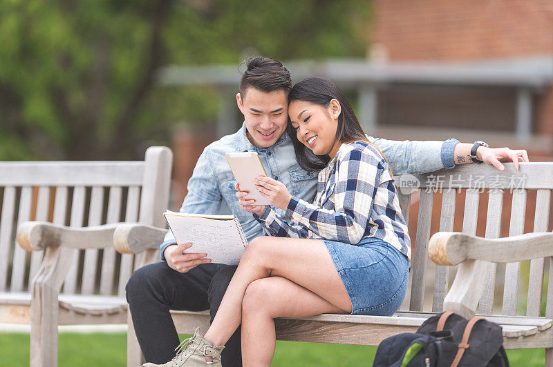 一对深情的年轻亚洲夫妇坐在公园的长椅上看一些有趣的平板电脑