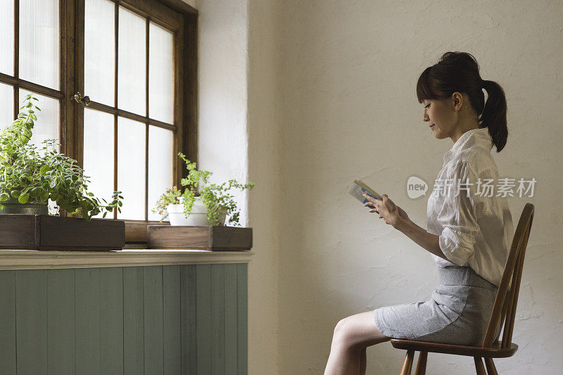 一个年轻的女人在一个房间的窗边看书