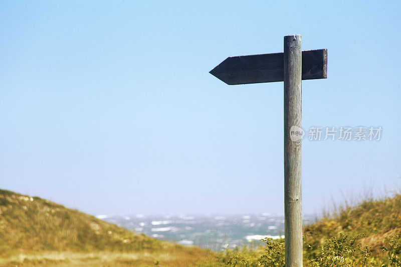 木制的步道路标，有清澈的蓝天和海景背景。