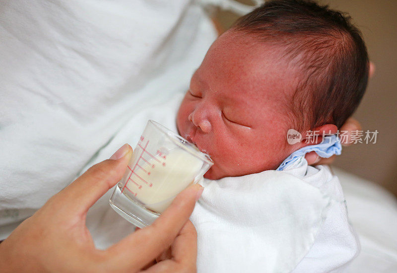 母亲用玻璃杯给婴儿喂奶。