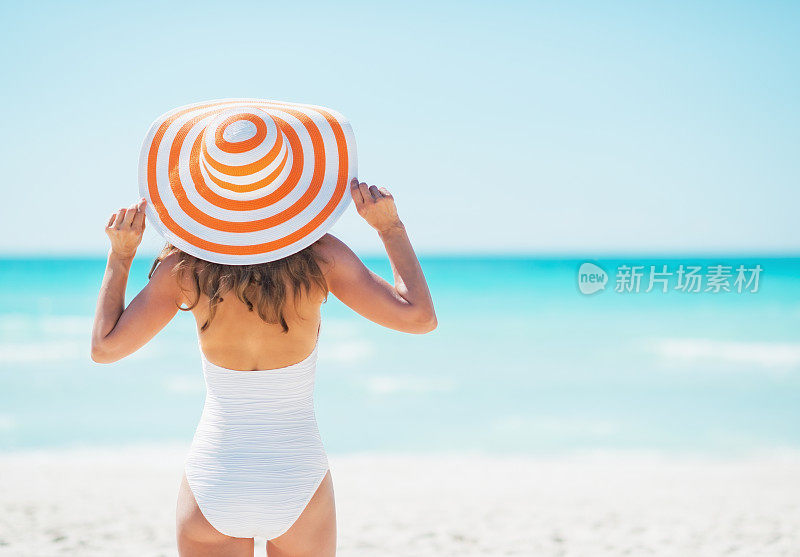 戴着帽子的年轻女子站在海滩上。后视