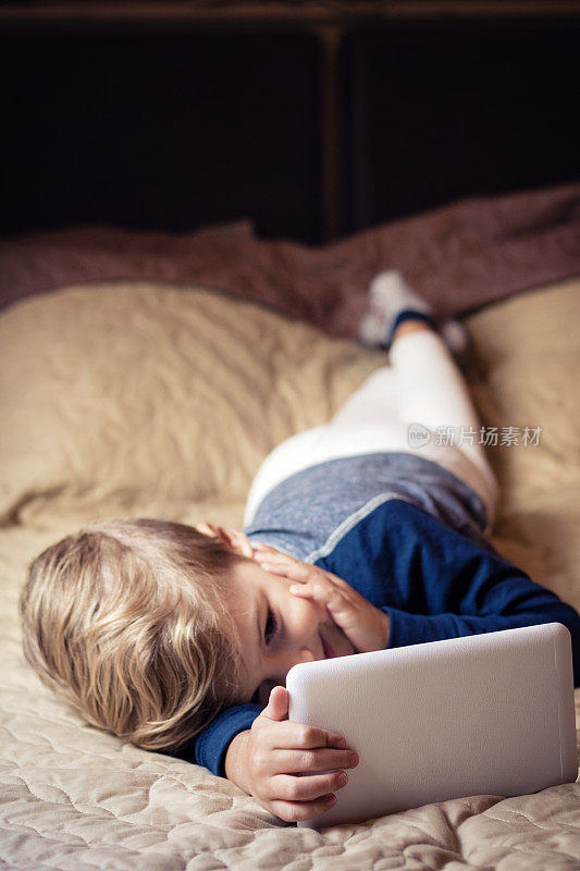 小孩子在床上休息，使用数码平板电脑。