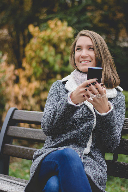 美丽的年轻女子使用手机在城市公园在秋天