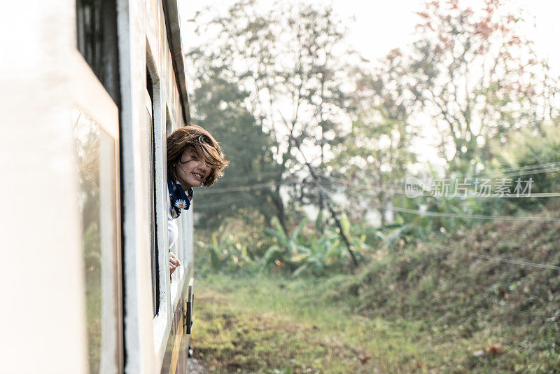 在泰国乘火车旅行的快乐女人从窗口望出去。