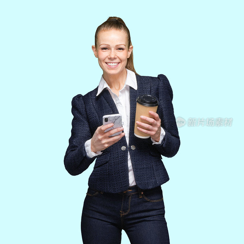 z一代女性穿着牛仔裤站在彩色背景前，拿着咖啡杯，用着智能手机