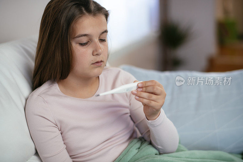 生病的小女孩在床上与温度计库存照片