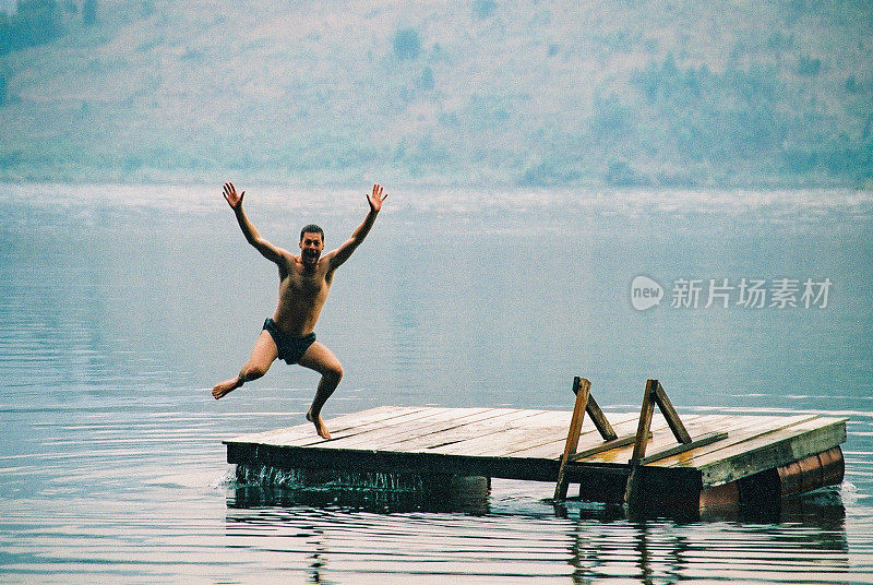 湖中浮动码头平台上的男子双手在空中跳跃