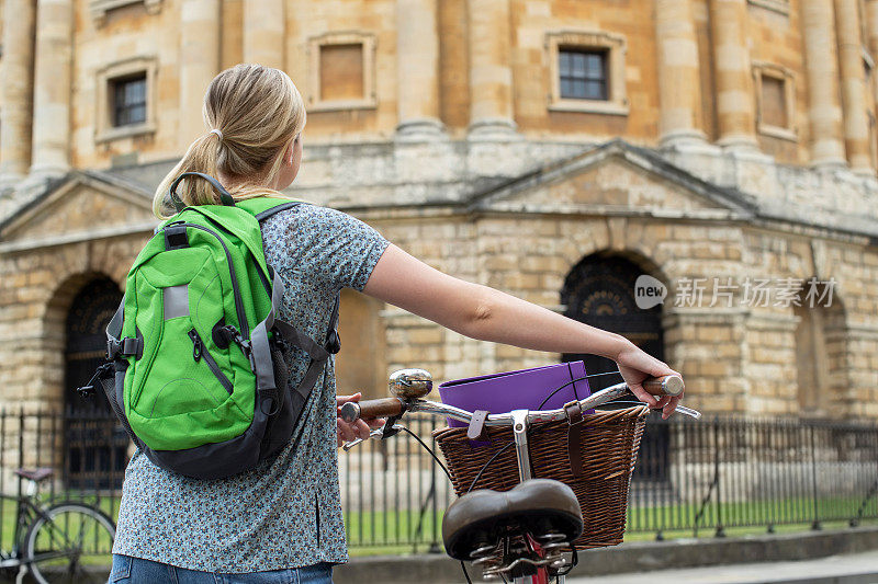 在英国拉德克里夫广场，女学生骑着老式自行车绕着牛津大学大楼的后视图
